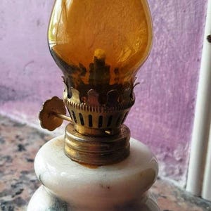 May include: A small, white marble oil lamp with a gold-colored metal base and a clear amber glass chimney.