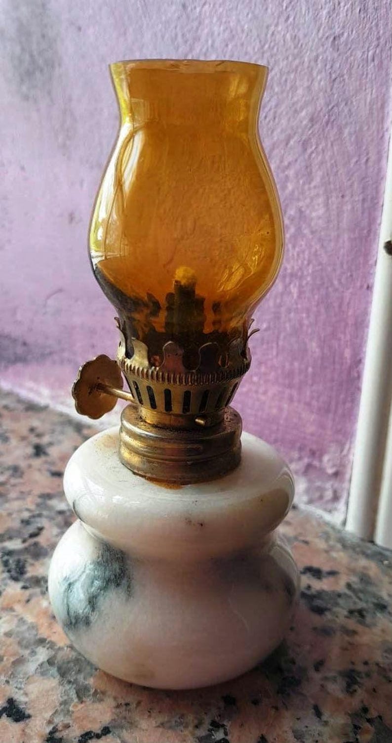 May include: A small, white marble oil lamp with a gold-colored metal base and a clear amber glass chimney.