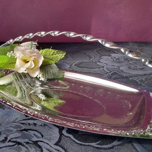 Peut inclure: Un plateau de service en argent avec une poignée torsadée et une bordure décorative. Un petit arrangement de fleurs artificielles est sur le plateau.