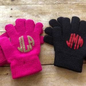 May include: Two pairs of fingerless gloves with monogrammed initials. One pair is pink with gold glitter initials "JLA" and the other pair is black with red initials "JMM".