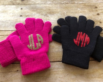 Puede incluir: Dos pares de guantes sin dedos con iniciales monogramadas. Un par es rosa con iniciales de purpurina dorada "JLA" y el otro par es negro con iniciales rojas "JMM".