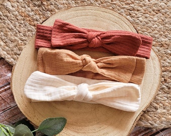 May include: Three fabric headbands in a set. The headbands are tied in a bow and are in shades of beige, brown, and rust.