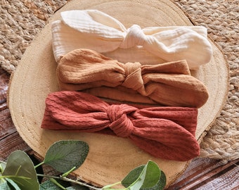 May include: Three fabric headbands in a set. The headbands are tied in a bow and are in shades of beige, brown, and rust.