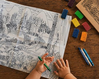 Könnte beinhalten: Ein großes weißes Malblatt aus Papier mit einer detaillierten schwarzen Strichzeichnung einer Waldlandschaft mit Bäumen, Bergen und einem Fluss. Ein grüner Buntstift wird in der Hand gehalten, daneben liegen bunte Wachsmalstifte.