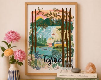 May include: A framed art print titled Tofino featuring a landscape illustration of a beach, forest, mountains, and a yellow camper van under a sunset sky. The print is displayed with a vase of pink flowers and a stack of three books.