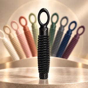 May include: A black cylindrical massage tool with a textured, spiked surface and a circular loop at the top. The tool is positioned vertically in the center, with a blurred array of identical tools in various colors arranged in a semi-circle behind it.
