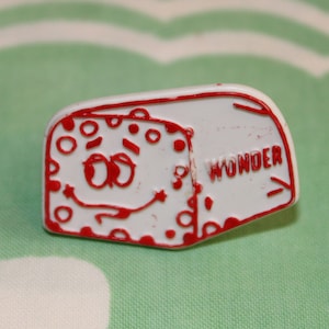 May include: White plastic Wonder Bread tag with red lettering and a cartoon face with googly eyes. The tag says "Wonder" in red letters.