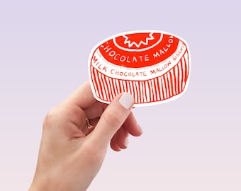 May include: A red and white sticker in the shape of a biscuit is held in a hand. The sticker has the words "Milk Chocolate Mallow Biscuit" printed on it. The design features a starburst pattern and vertical lines.