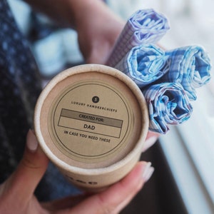 May include: A brown cardboard tube with a label that says "5 Luxury Handkerchiefs, Created For: Dad, In Case You Need These". The tube is filled with a stack of blue and white checkered handkerchiefs.