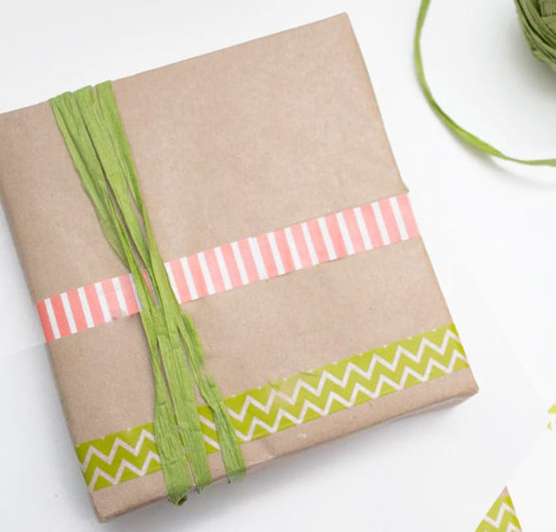May include: A brown paper gift box wrapped with green and pink patterned washi tape. The box is tied with green shredded paper.