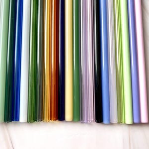 May include: A collection of colorful glass straws in various shades, including clear, green, blue, yellow, and purple. The straws are arranged vertically, showcasing their smooth, cylindrical shape. These reusable straws offer an eco-friendly alternative to plastic.