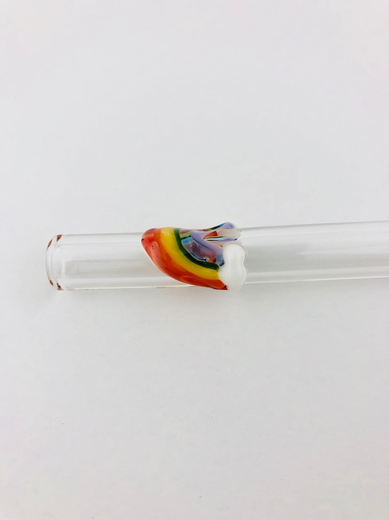 May include: A clear glass tube featuring a decorative accent piece shaped like a rainbow. The accent is crafted from multi-colored glass, displaying bands of red, orange, yellow, green, blue, and violet, finished with a solid white glass end.