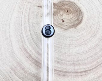 Può includere: Una cannuccia in vetro trasparente con un elemento decorativo sferico bianco e nero, caratterizzata dal numero otto stampato in nero su uno sfondo circolare bianco, posizionato centralmente sul corpo cilindrico della cannuccia.