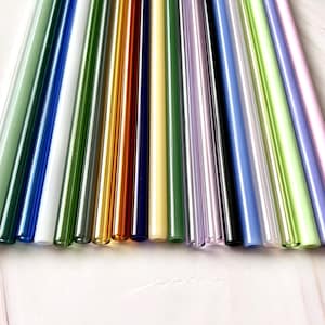 May include: A collection of colorful glass straws in various shades, including green, blue, yellow, and pink. The straws are arranged in a diagonal pattern, showcasing their vibrant colors and smooth, cylindrical shape. These reusable straws are a sustainable alternative.
