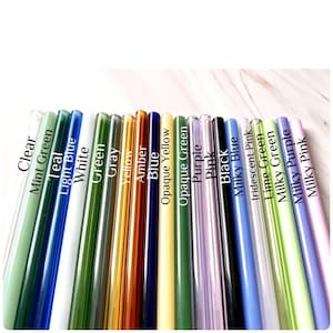 May include: A collection of colorful glass straws in various shades, including clear, green, blue, yellow, purple, and pink. Each straw is labeled with its color name in white text. The straws are arranged diagonally.