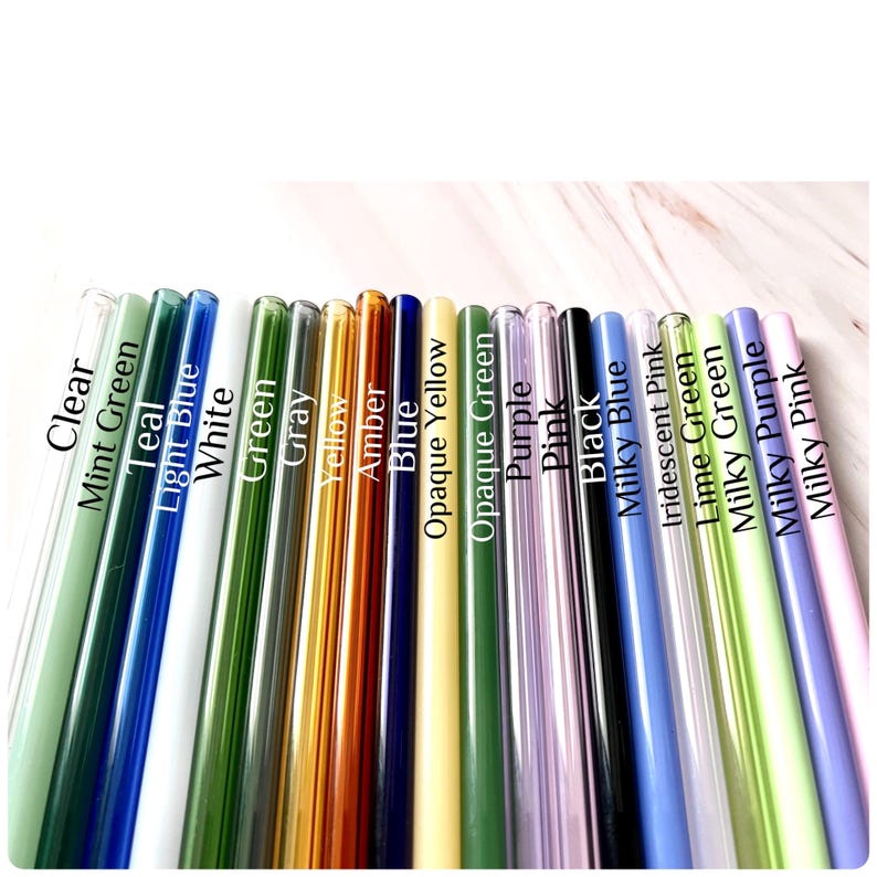 May include: A collection of colorful glass straws in various shades, including clear, green, blue, yellow, purple, and pink. Each straw is labeled with its color name in white text. The straws are arranged diagonally.