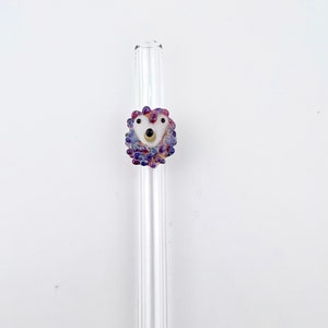 Peut inclure: Une paille &agrave; boire en verre transparent avec une perle en verre violette et blanche en haut. La perle est en forme de c&oelig;ur et a un visage blanc avec des yeux noirs et un nez dor&eacute;.