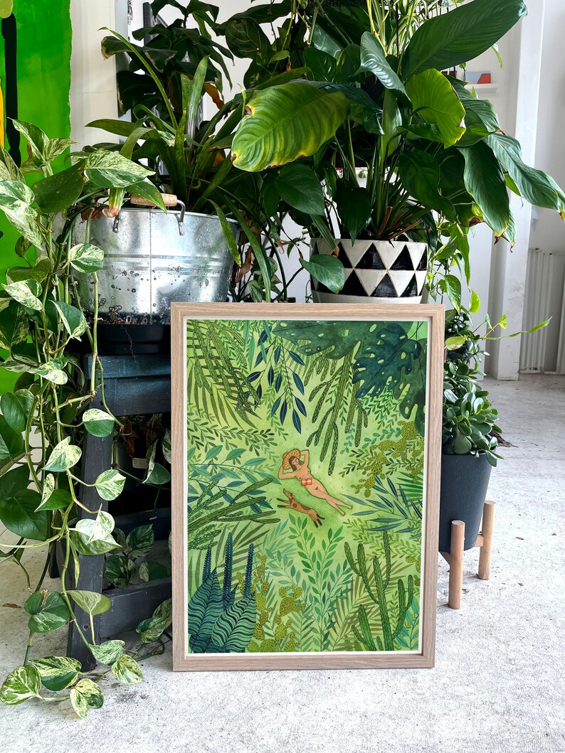 Pu&ograve; includere: Un'illustrazione incorniciata di una donna sdraiata in una lussureggiante giungla verde con un cane al suo fianco. L'illustrazione &egrave; circondata da una cornice marrone chiaro.