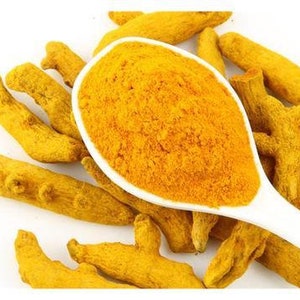 Peut inclure: Une cuillère en céramique blanche remplie de poudre de curcuma jaune vif, entourée de morceaux de racine de curcuma.