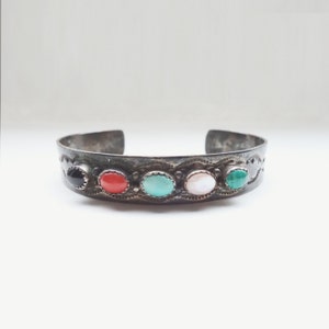May include: A silver cuff bracelet with five oval-shaped gemstones. The stones are black, red, turquoise, white, and green.