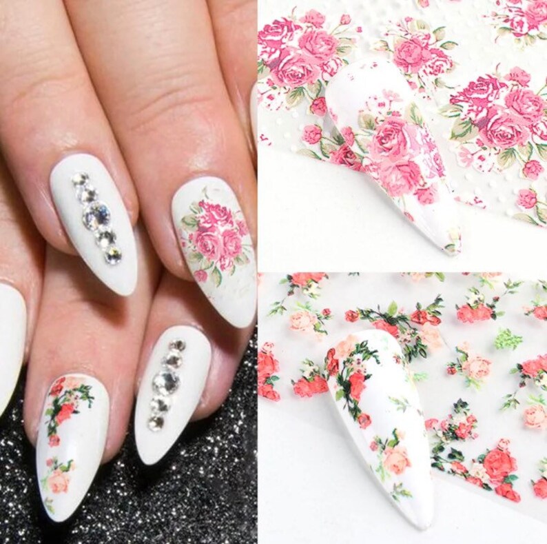 Puede incluir: Calcoman&iacute;as para u&ntilde;as con un dise&ntilde;o floral que presenta rosas rosadas y hojas verdes sobre un fondo blanco. Las calcoman&iacute;as se muestran aplicadas a un conjunto de puntas de u&ntilde;as blancas.