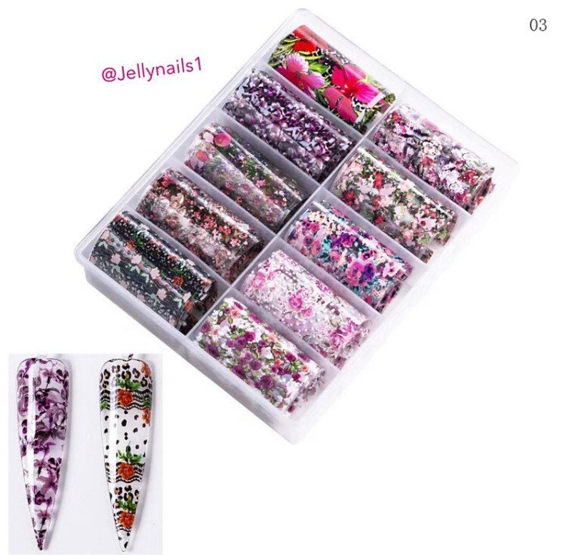 Puede incluir: Una caja de pl&aacute;stico transparente llena de 12 rollos de l&aacute;mina de transferencia para el arte de las u&ntilde;as. Cada rollo tiene un patr&oacute;n floral diferente en tonos de rosa, morado y verde. La caja est&aacute; etiquetada con el n&uacute;mero "03" y el texto "@Jellynails1".