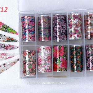 Puede incluir: Un conjunto de 12 rollos de l&aacute;mina de transferencia para el arte de las u&ntilde;as. La l&aacute;mina es plateada y tiene una variedad de patrones florales. Los rollos est&aacute;n en un contenedor de pl&aacute;stico transparente con la etiqueta "F12".