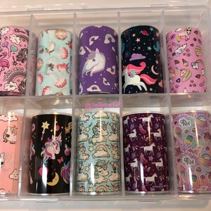 May include: A set of 10 unicorn-themed nail art foils in a clear plastic storage box. The foils feature various designs including unicorns, rainbows, stars, and hearts. The foils are in a variety of colours including pink, purple, blue, and black.