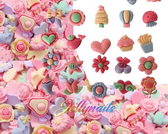 May include: A collection of pastel-colored resin embellishments, including flowers, hearts, bows, and food-themed charms. The assortment features various shapes and sizes, with a mix of pink, green, and lavender hues. The image includes the text "Jellynails".