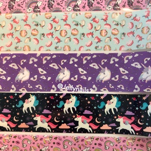 May include: Five different patterned strips of nail art decals featuring unicorns, rainbows, stars, and hearts. The patterns are on a pink, light blue, purple, black, and pink background.
