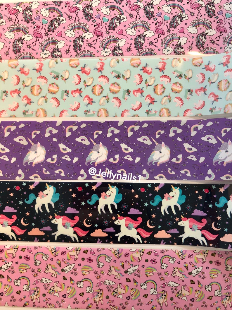 May include: Five different patterned strips of nail art decals featuring unicorns, rainbows, stars, and hearts. The patterns are on a pink, light blue, purple, black, and pink background.