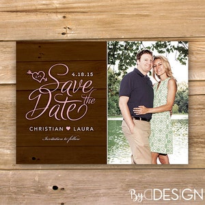 Op de afbeelding: Save the Date kaart met een rustieke houten achtergrond. De kaart heeft een roze hart met een pijl en de tekst "Save the Date" in roze schrift. De datum "4.18.15" is in zwart gedrukt. De namen "Christian" en "Laura" zijn in zwart gedrukt met een roze hart ertussen. De tekst "Invitation to follow" is in zwart gedrukt. Een foto van een stel is te zien aan de rechterkant van de kaart.
