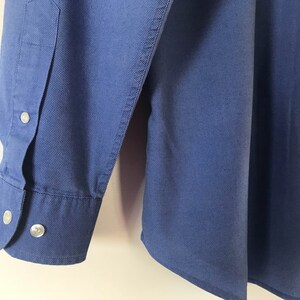 May include: A blue long-sleeved button-down shirt with a single button cuff.