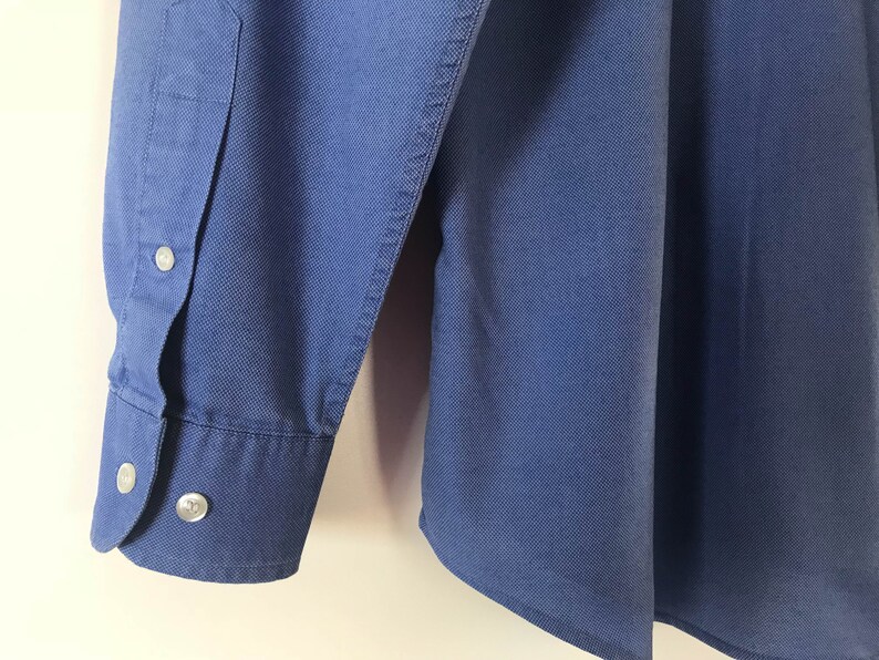 May include: A blue long-sleeved button-down shirt with a single button cuff.