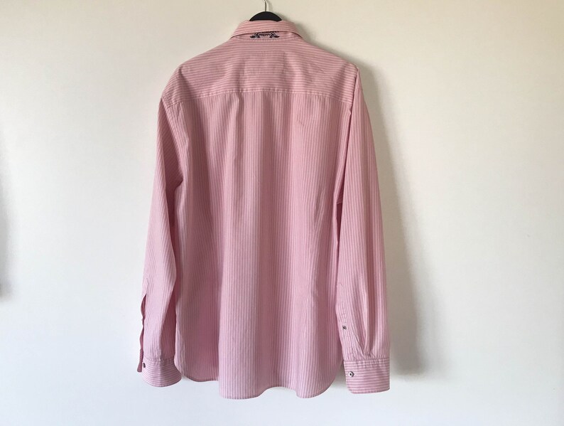 May include: A pink and white striped long-sleeve button-down shirt with a small embroidered design on the collar.