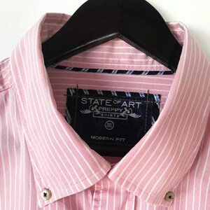 May include: Pink and white striped dress shirt with a black label that says "State of Art Preppy Shirts" and "Modern Fit". The shirt has a button-down collar and is size XXL.