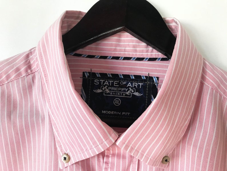 May include: Pink and white striped dress shirt with a black label that says "State of Art Preppy Shirts" and "Modern Fit". The shirt has a button-down collar and is size XXL.