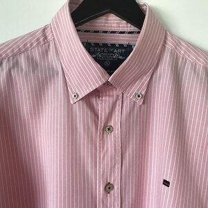 May include: A pink and white striped long-sleeve button-down shirt with a State of Art Preppy Shirts label. The shirt has a button-down collar and a small logo on the left chest.