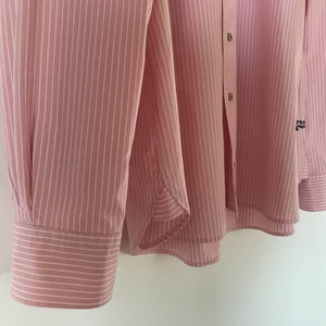 May include: A pink and white striped long-sleeved shirt with a button-up front and a small logo on the right sleeve.