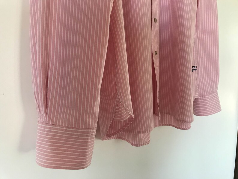 May include: A pink and white striped long-sleeved shirt with a button-up front and a small logo on the right sleeve.