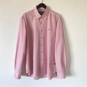 May include: A pink striped long-sleeve button-down shirt with a small logo on the left chest.