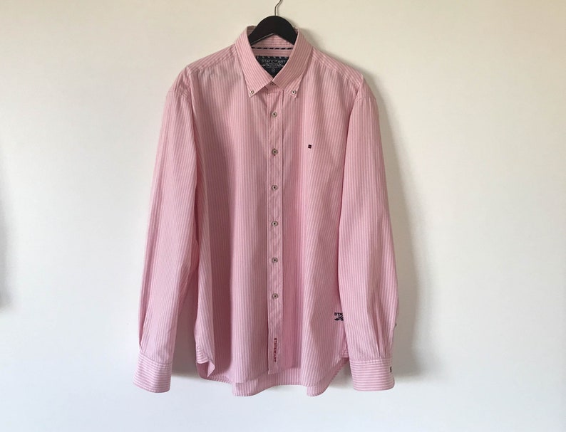 May include: A pink striped long-sleeve button-down shirt with a small logo on the left chest.