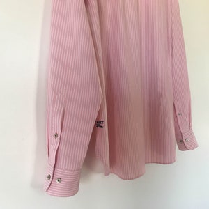 May include: A pink and white striped long-sleeved shirt with a small embroidered logo on the left sleeve. The logo says "HART OF" with a small mustache.