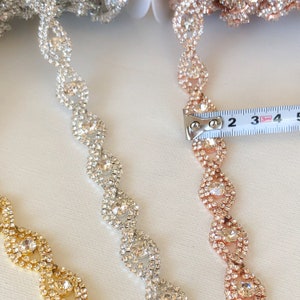 May include: Three strands of rhinestone trim, one gold, one silver, and one rose gold. The trim is approximately 2 inches long and features a repeating pattern of oval-shaped rhinestones.