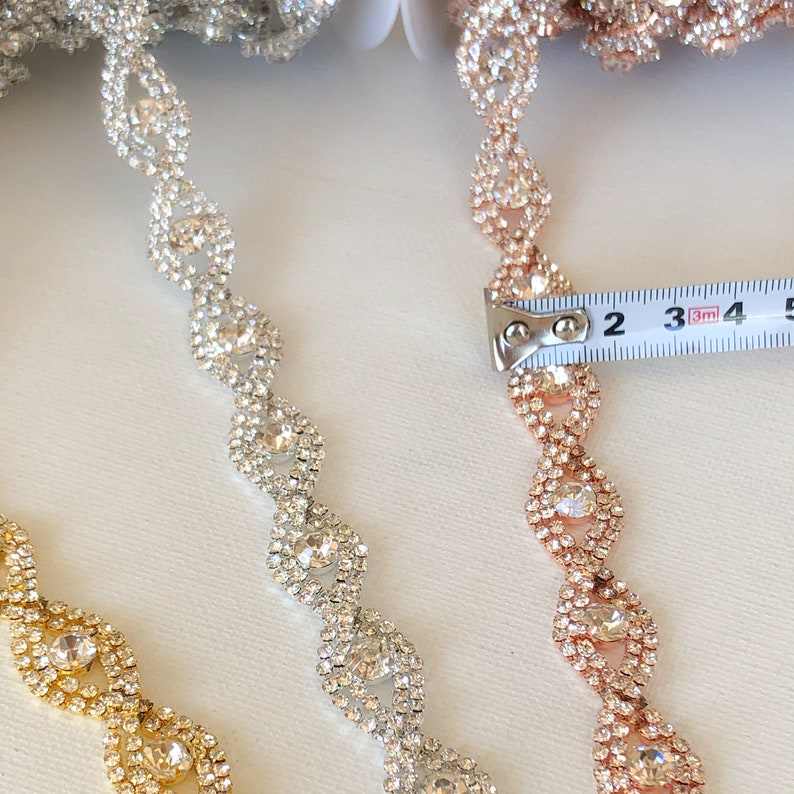 May include: Three strands of rhinestone trim, one gold, one silver, and one rose gold. The trim is approximately 2 inches long and features a repeating pattern of oval-shaped rhinestones.