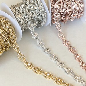 May include: Three spools of rhinestone trim in gold, silver, and rose gold. Each spool features a continuous chain of clear rhinestones in a wavy pattern.