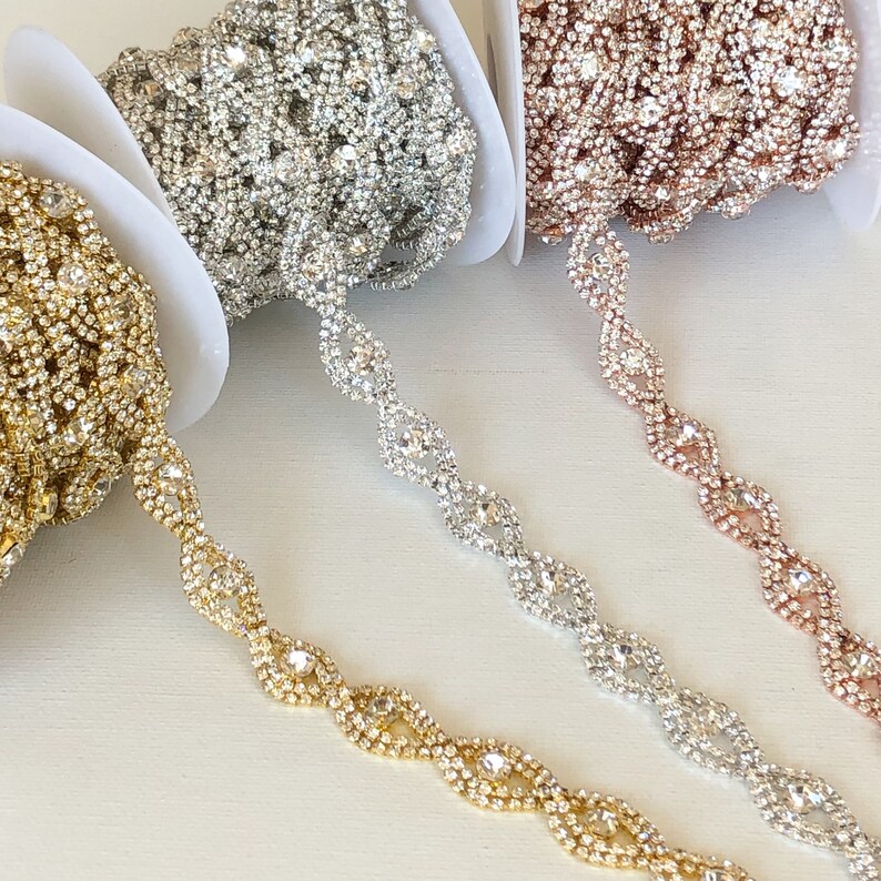 May include: Three spools of rhinestone trim in gold, silver, and rose gold. Each spool features a continuous chain of clear rhinestones in a wavy pattern.