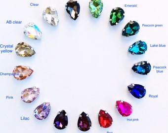 May include: A collection of teardrop-shaped rhinestones in various colors, including clear, gray, green, and pink. Each gem is set in a silver-colored metal base. The image displays a variety of colors, such as emerald, lake blue, and hot pink.