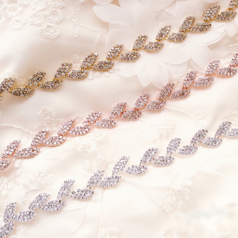 May include: Three rows of rhinestone trim with a leaf design. The trim is available in gold, rose gold, and silver.