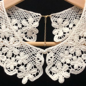 May include: White crocheted lace collar with a pearl button and a gold chain closure.